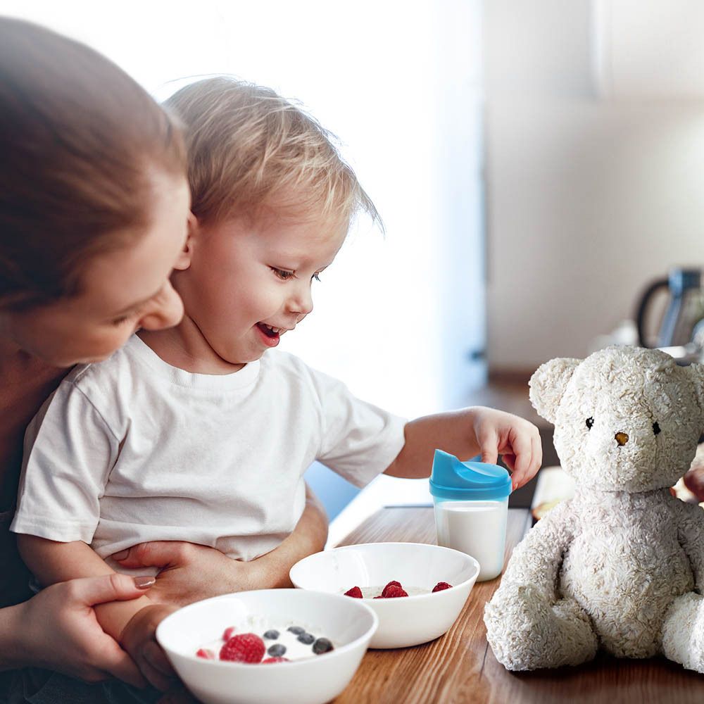 Mère et enfant à table. Enfant avec gobelet. Bols de fruits. Ours en peluche.