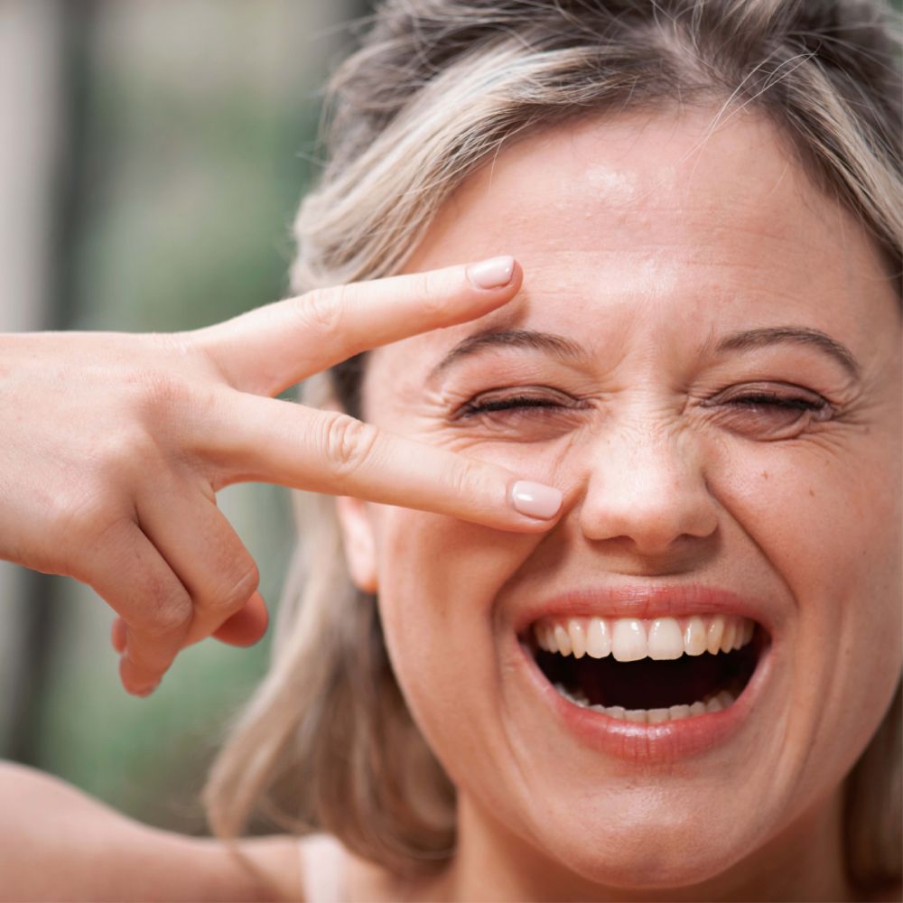 Femme avec les yeux fermés, main formant un V. SVR AMPOULE REFRESH.