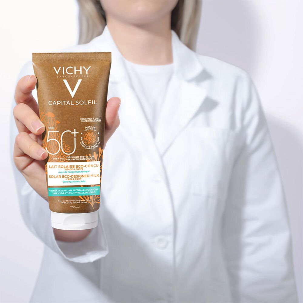 Persoon houdt een zonnebrandmelk tube vast. Opschrift: VICHY, CAPITAL SOLEIL, SPF 50+. Lait Solaire Eco-Conçu.