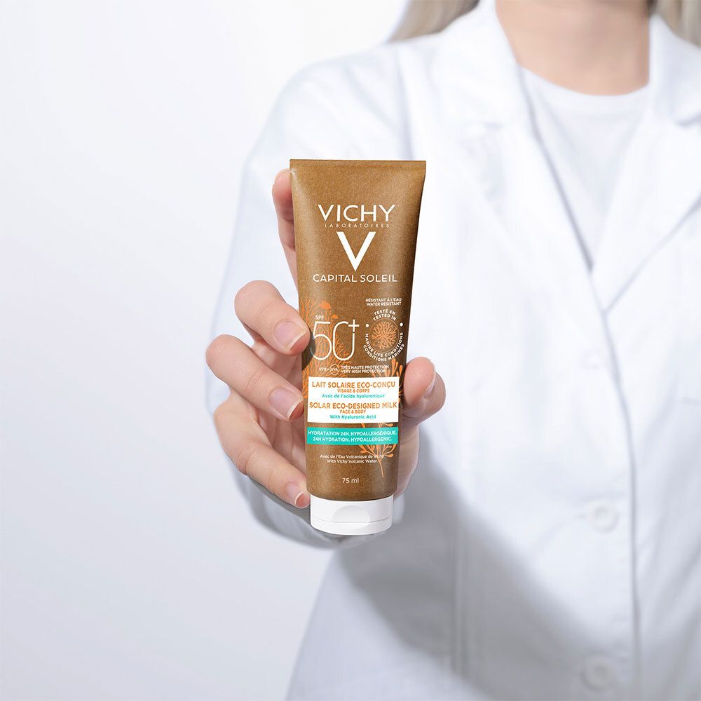 Persoon houdt zonnebrandmelk tube Vichy Capital Soleil SPF 50+ vast. Bruine tube, witte dop. Opschrift en logo zichtbaar.