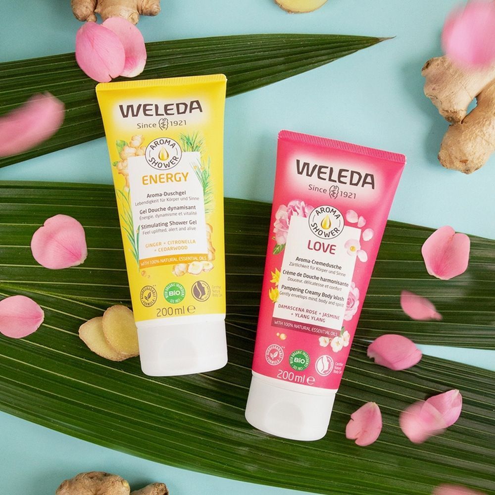 Twee tubes "WELEDA" douchegel: Geel "ENERGY" en roze "LOVE". Bloemblaadjes en stukjes gember ernaast. 200ml.