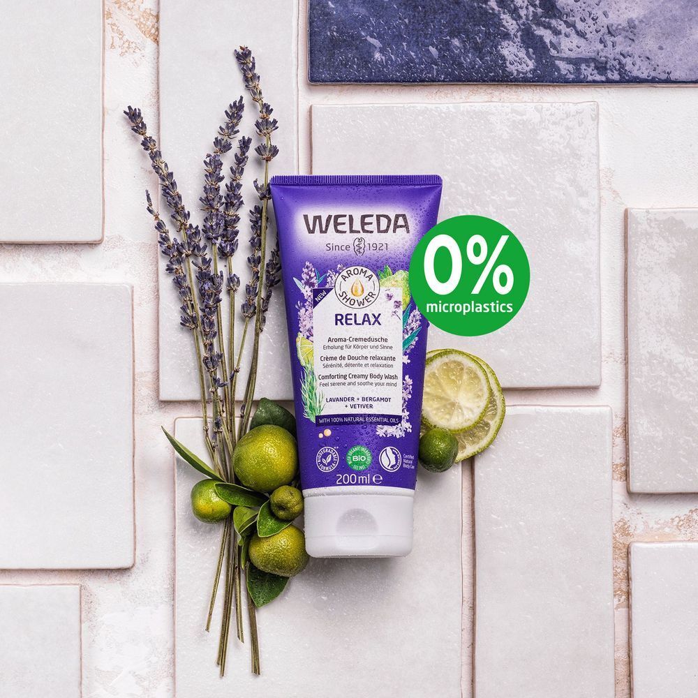 Paarse tube met witte dop, omringd door lavendel, limoenen en bladeren. Tekst: WELEDA, Aroma Shower Relax, 200ml, 0% microplastics.