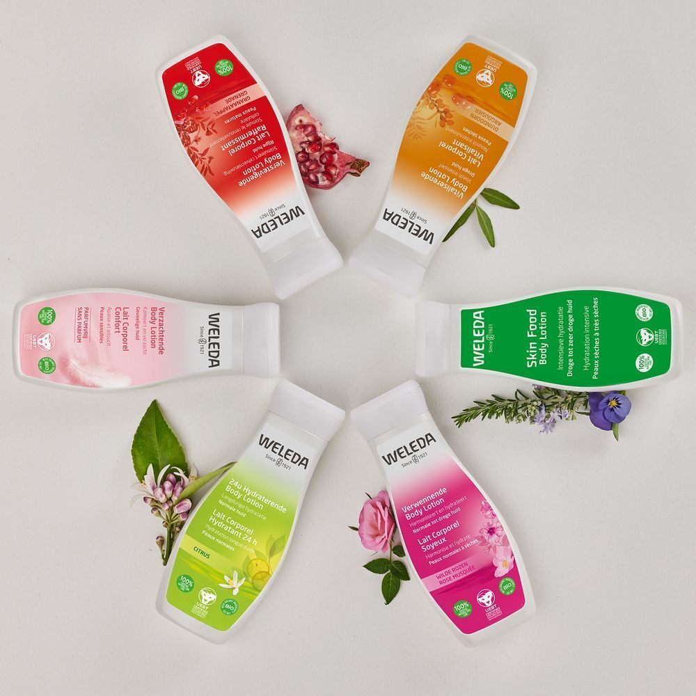Zes flessen bodylotion, verschillende kleuren, in een cirkel gerangschikt. Merk: WELEDA. Labels met tekst.
