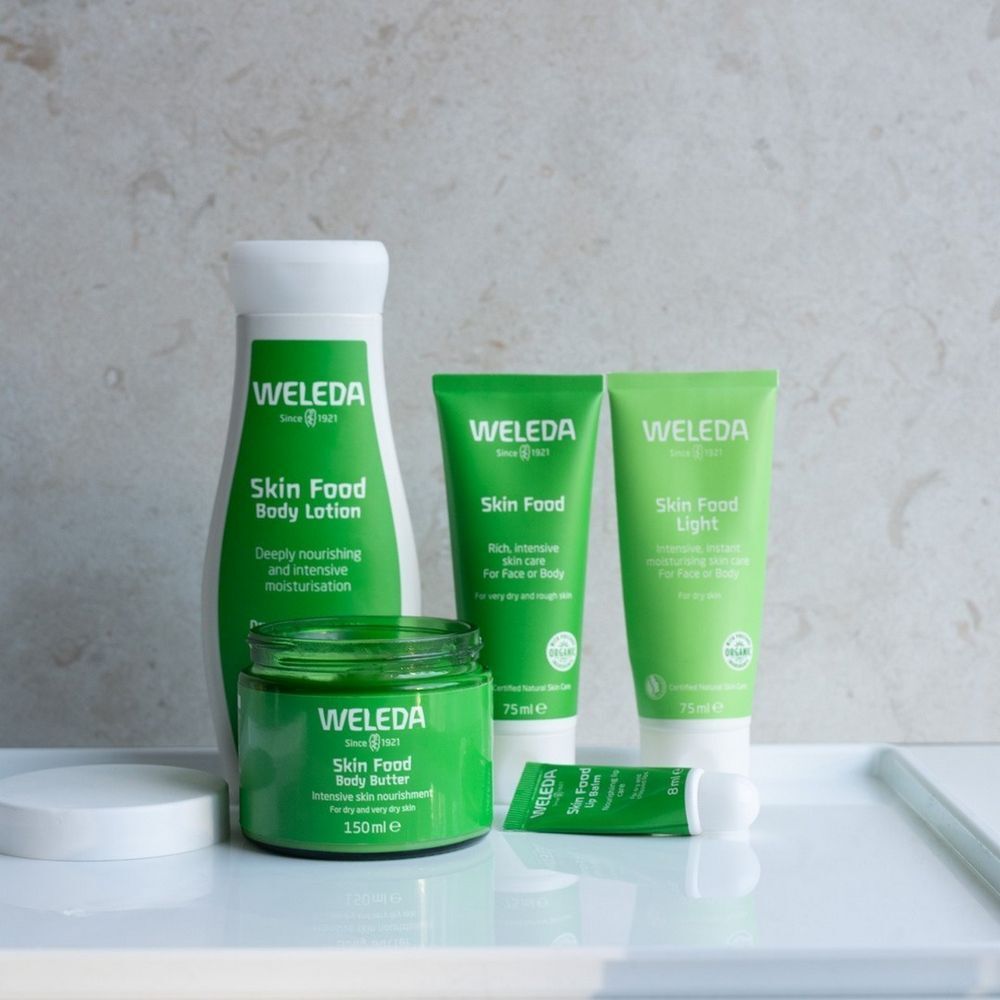 Verschillende groene Weleda-producten op wit dienblad. Bevat: Body Lotion, Skin Food, Skin Food Light, Skin Food Body Butter.