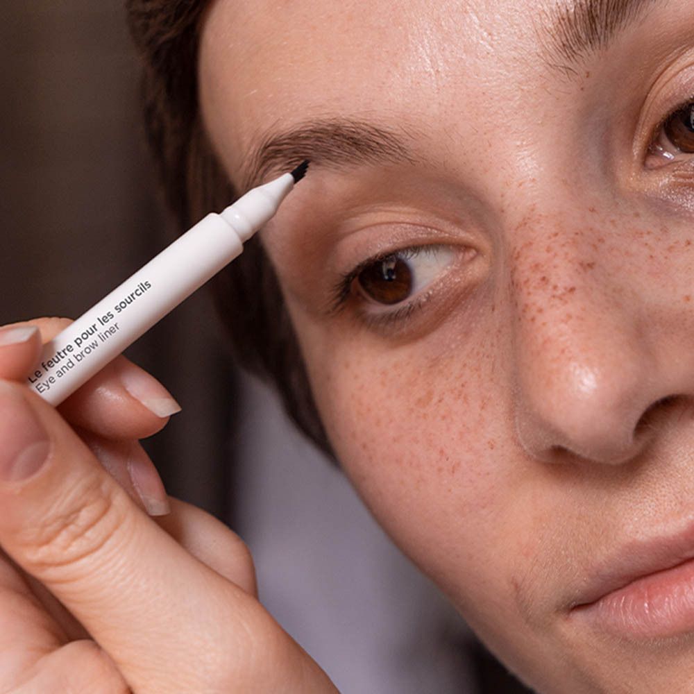 Gros plan : personne dessine sourcil avec feutre MÊME. Eye and brow liner. Application.