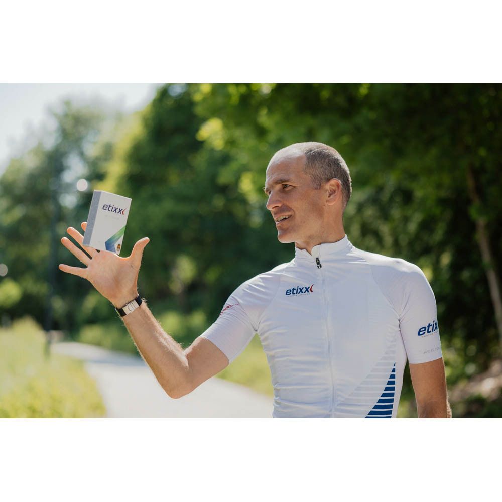 Man houdt een kleine doos "etixx" vast. Hij draagt een wit wielershirt.