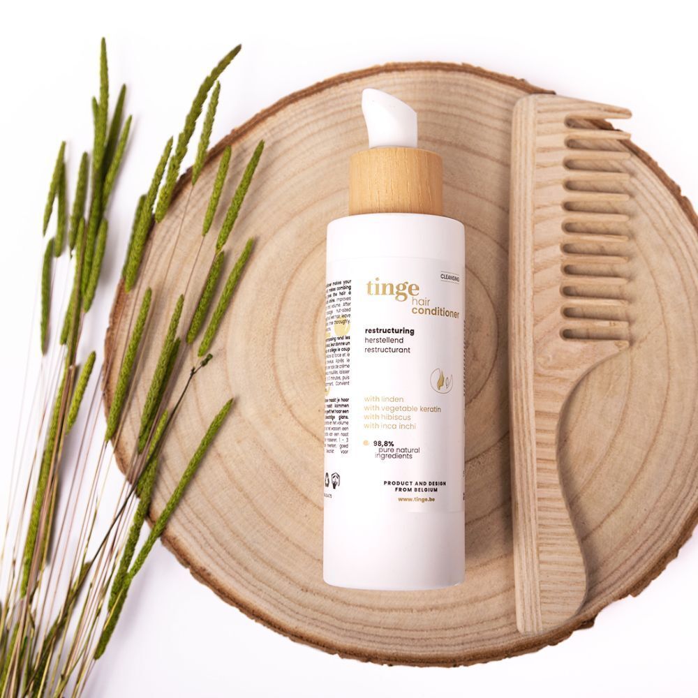 Flacon avec bouchon en bois et pompe sur rondin de bois avec peigne et plantes. Inscription: tinge hair conditioner.
