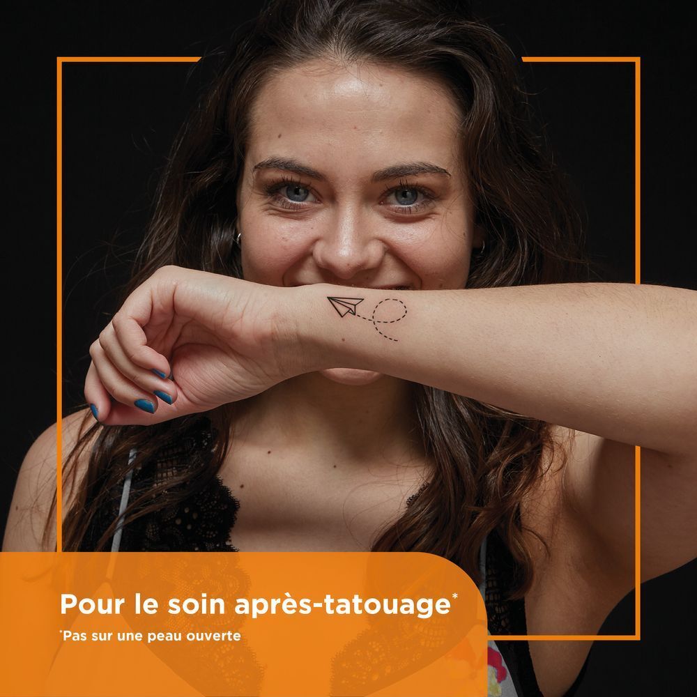 Femme avec tatouage au poignet. Texte: Pour le soin après-tatouage. Ne pas appliquer sur peau ouverte.