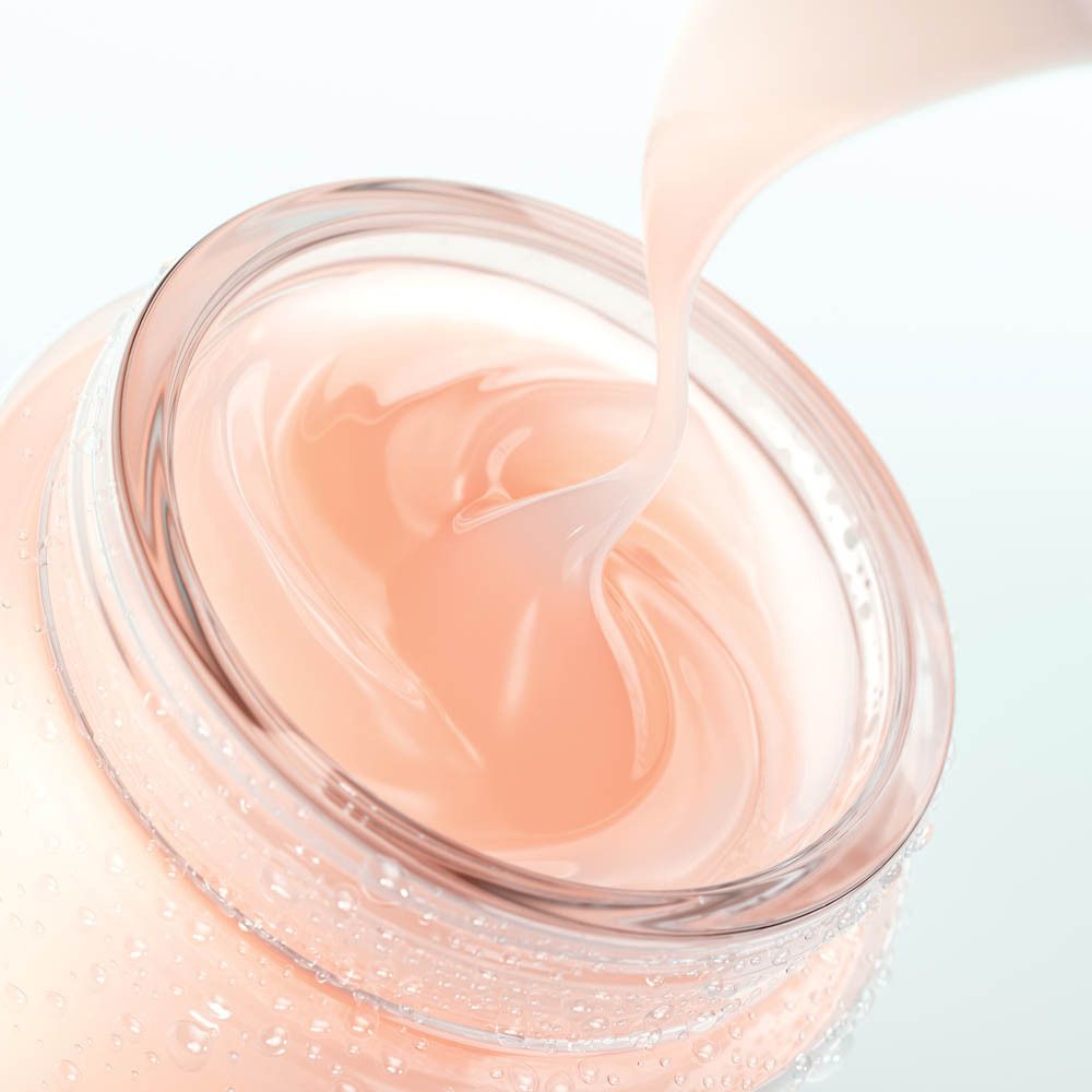 Ein Glasbehälter mit einer zartrosa Creme, die aus einem Spatel gegossen wird.