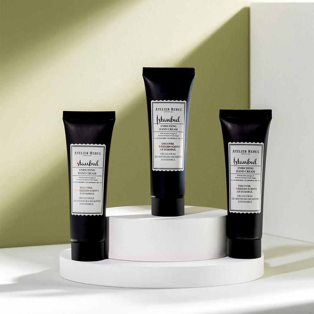 Drei schwarze Tuben mit weißem Etikett auf einer weißen Plattform. Text: ATELIER REBUL Istanbul, Enriching Hand Cream.