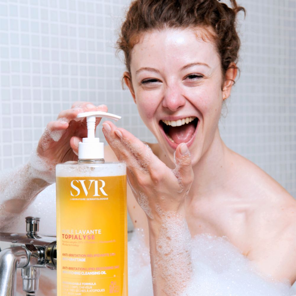 Femme dans une baignoire tenant un flacon SVR Huile Lavante Topialyse. Mousse autour d'elle.