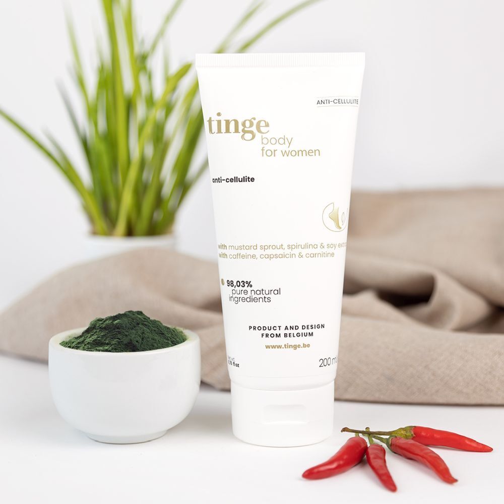 Weiße Tube mit Produktbeschriftung: tinge body for women, anti-cellulite, 98,03% natürliche Inhaltsstoffe. Schale mit grünem Pulver, rote Chili.