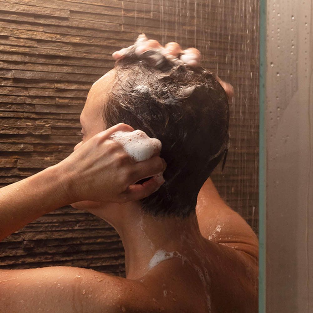 Persoon wast haar haar onder de douche. Schuim op het hoofd.