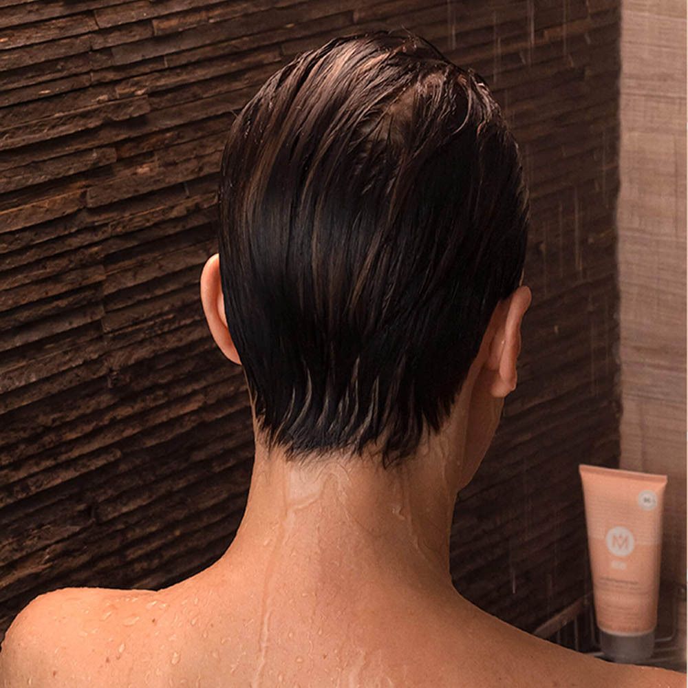Vue arrière d'une personne sous la douche. Cheveux mouillés, tube de shampooing en arrière-plan.