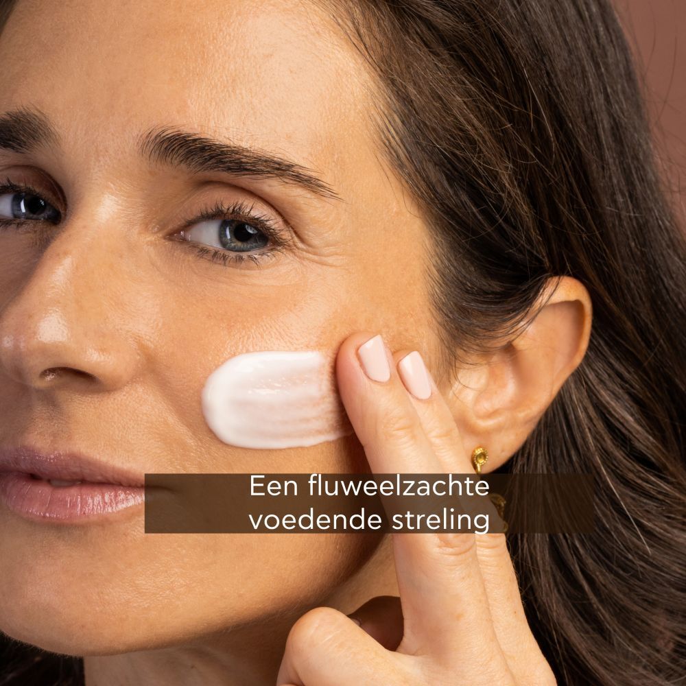 Vrouw brengt crème aan. Tekst: Een fluweelzachte voedende streling.