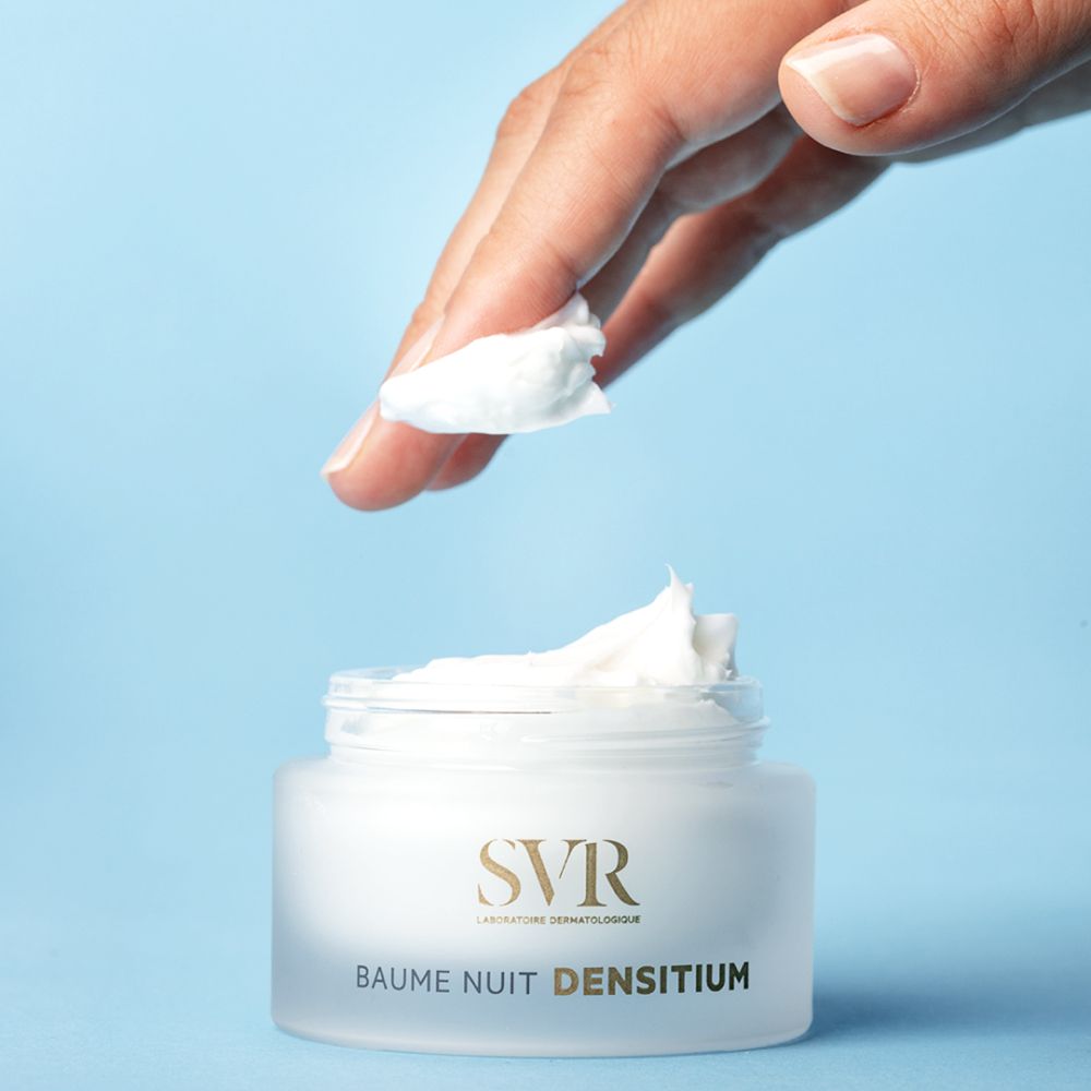Hand houdt product vast. Product is een witte pot met deksel. Op de pot staat "SVR" en "BAUME NUIT DENSITIUM".