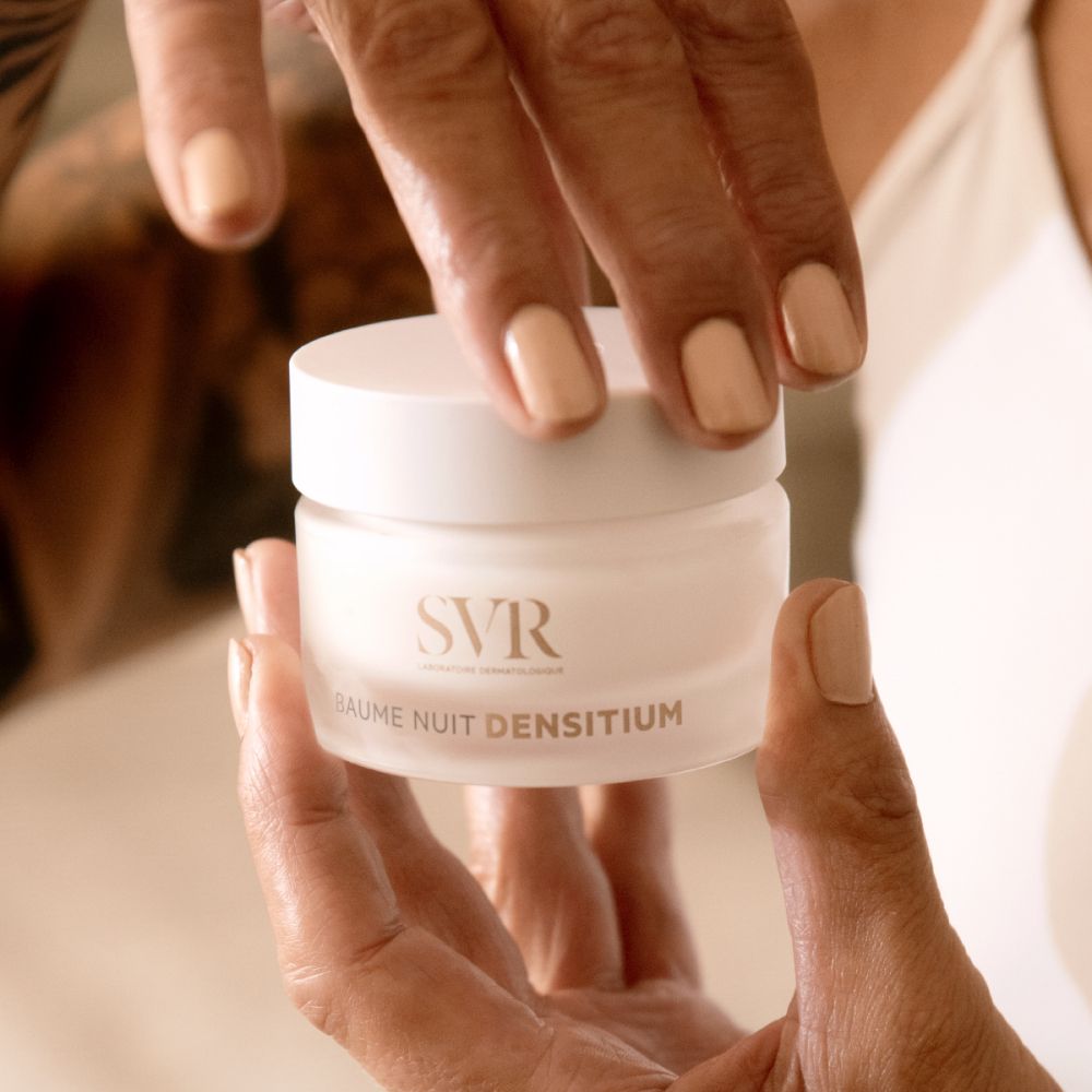 Handen houden product vast. Product is een witte pot met deksel. Op de pot staat "SVR" en "BAUME NUIT DENSITIUM".