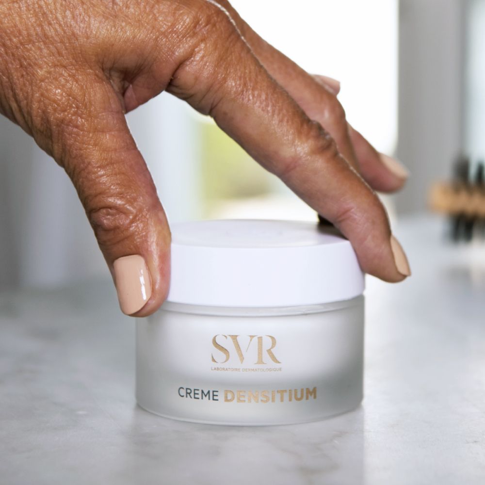 Hand houdt crèmepot vast. Op de pot staat "SVR" en "CREME DENSITIUM".
