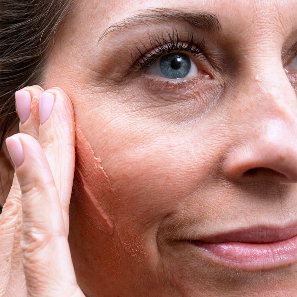 Vrouw brengt crème aan. Roze crème op gezicht.
