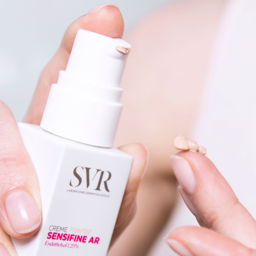 Close-up van een hand die crème uit een flesje haalt. Productnaam en logo zichtbaar.