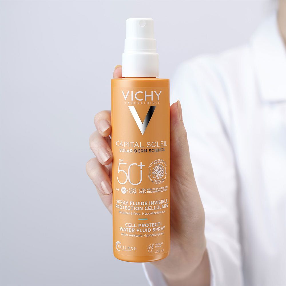 Hand die een oranje sprayfles vasthoudt. Opschrift: Vichy, Capital Soleil, SPF 50+.