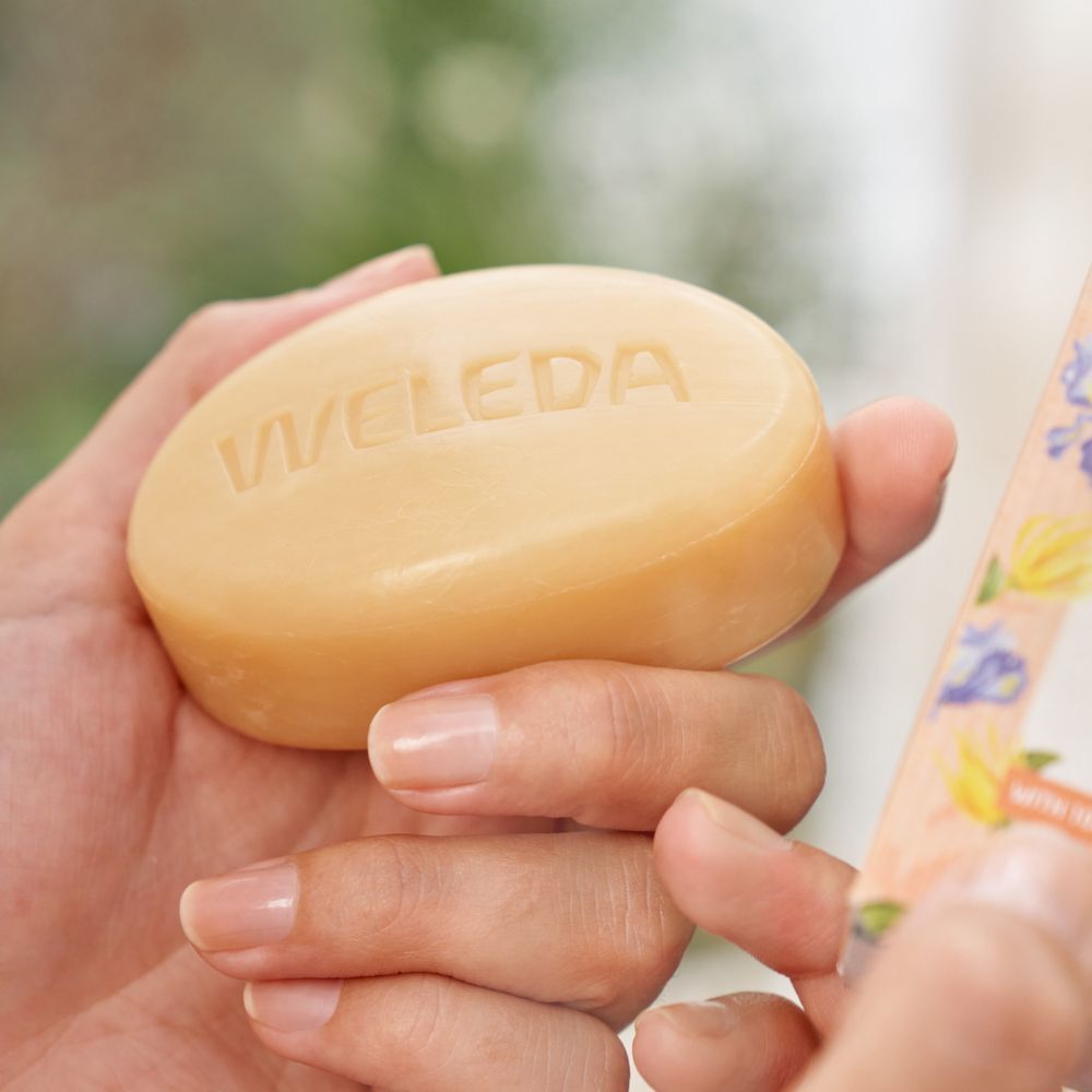 Handen houden zeep met Weleda-logo. Zeep met bloemmotieven en productnaam.