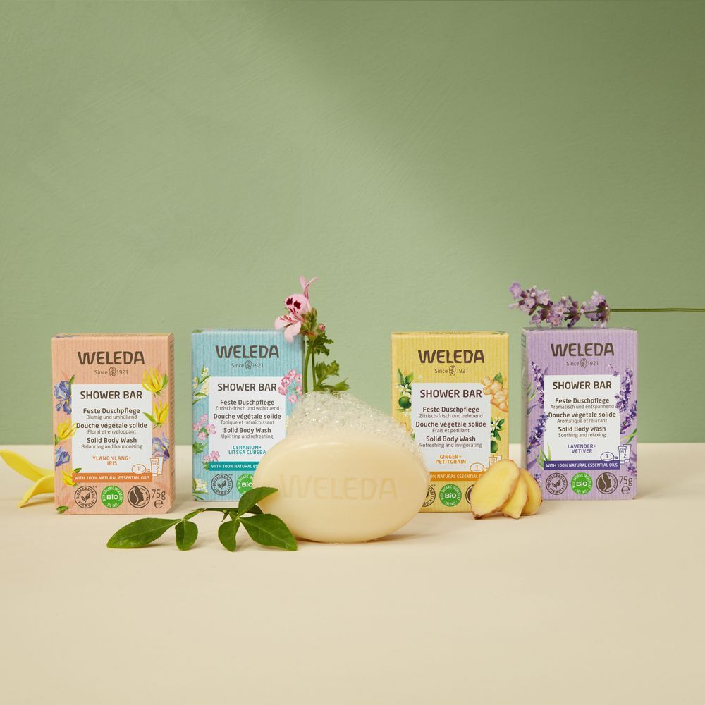 Meerdere zepen en verpakkingen. Zeep met schuim. Verpakkingen met "WELEDA"-logo en productnaam. Groene achtergrond.