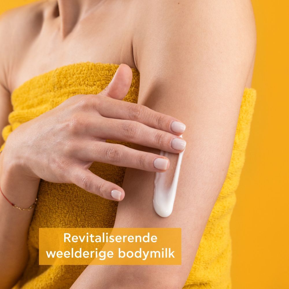 Persoon brengt product aan op arm. Gele achtergrond. Lait corps revitalisant.