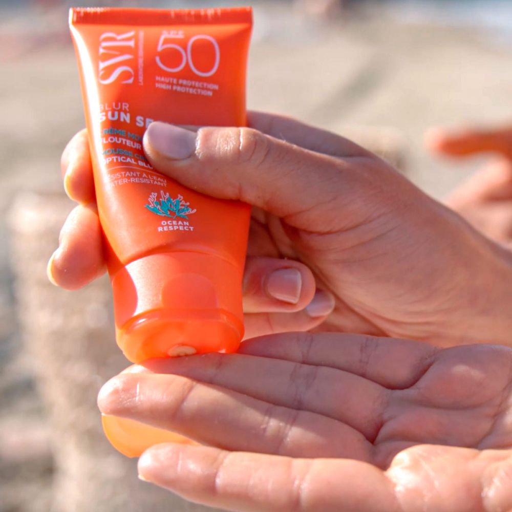 Mains tenant un tube orange SVR Sun Secure Blur LSF50+. Produit pressé sur la paume. SPF 50+.