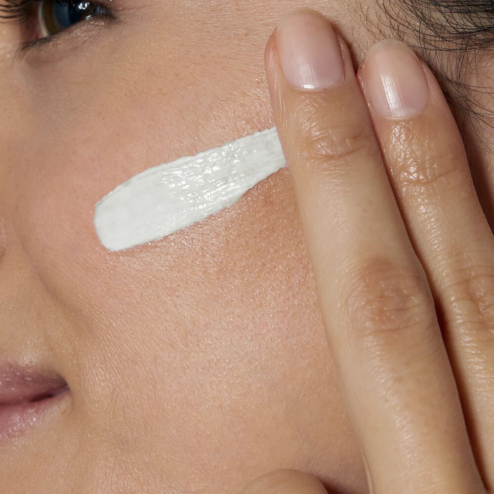 Close-up van een hand die crème op de wang aanbrengt. Witte crème wordt aangebracht.