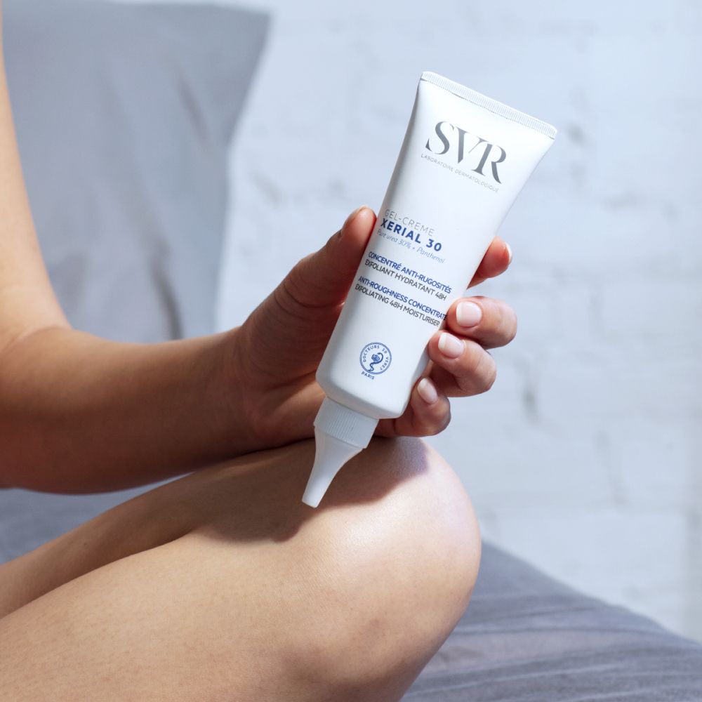 Personne applique SVR XERIAL 30 sur une jambe. Tube blanc. Fond blanc.