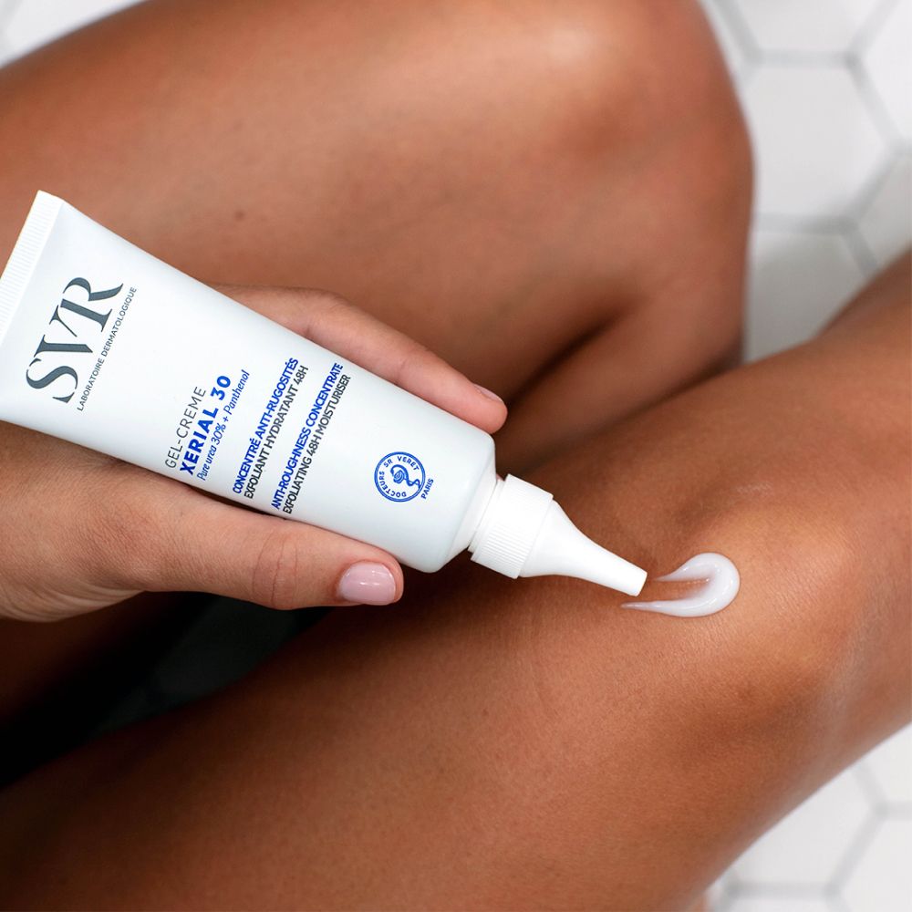 Application de SVR XERIAL 30 sur une jambe. Gel-crème sort du tube. Fond blanc.