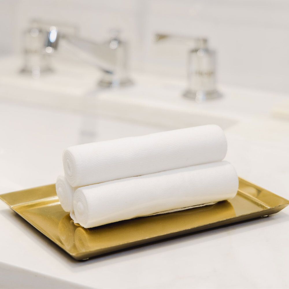Plateau doré avec trois rouleaux de bandages blancs. En arrière-plan, un lavabo avec un robinet.