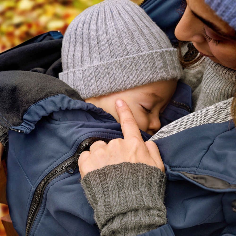 Gros plan d'un bébé dans une veste bleue. Une main touche doucement le visage du bébé. Bonnet gris.