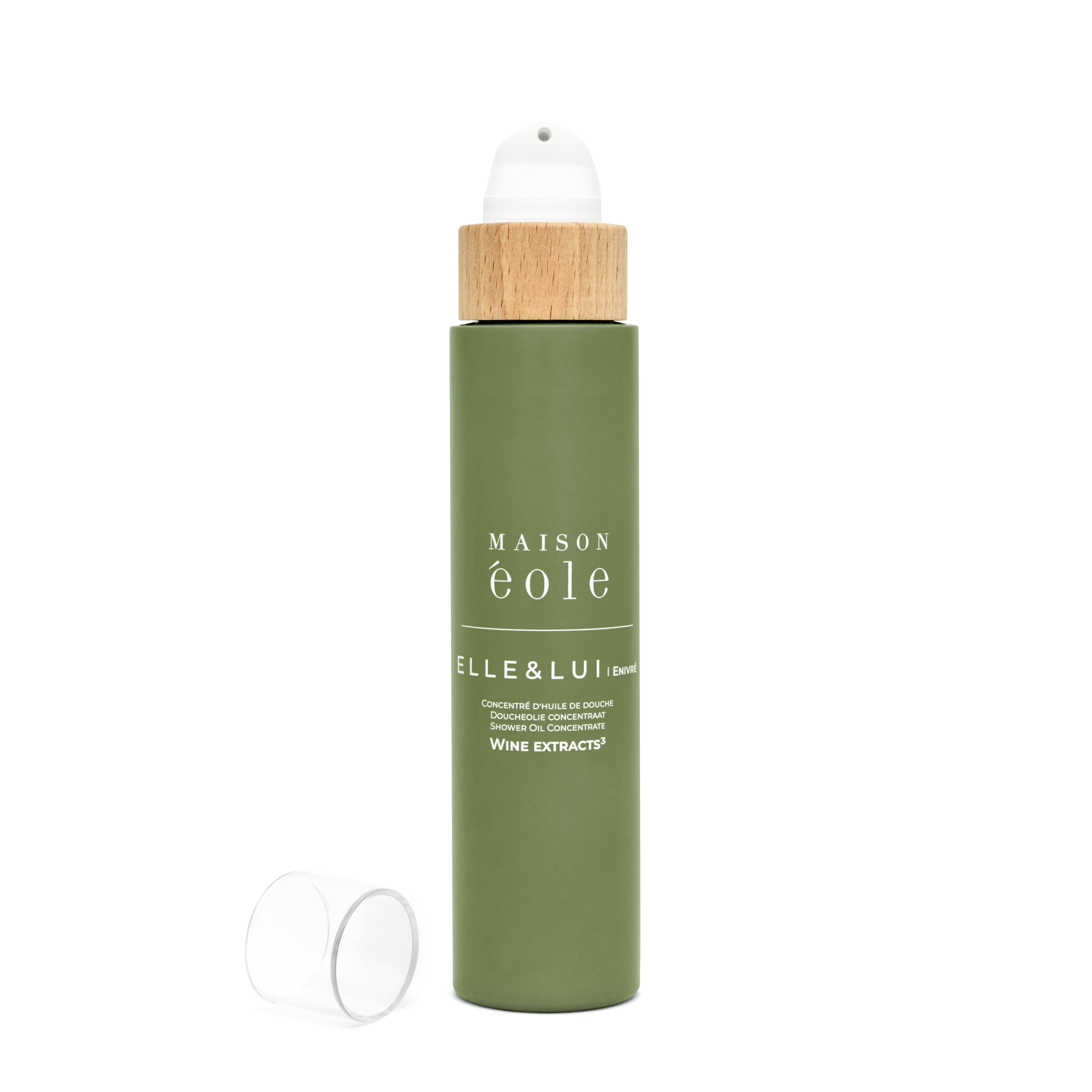 Grüne Flasche mit Sprühkopf und Holzdeckel, ohne Kappe. Aufschrift: Maison Éole, Elle & Lui, Concentré d'Huile de Douche.