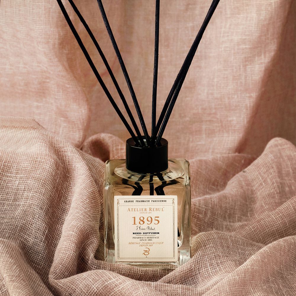 Glasdiffusor mit schwarzen Stäbchen. Aufschrift: ATELIER REBUL 1895. Auf rosa Stoff.