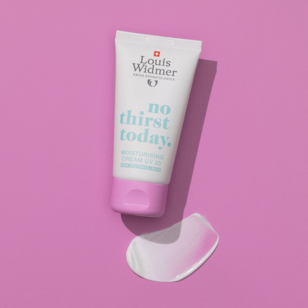 Tube blanc avec bouchon lilas et goutte de crème sur fond rose. Inscription: Louis Widmer, no thirst today.