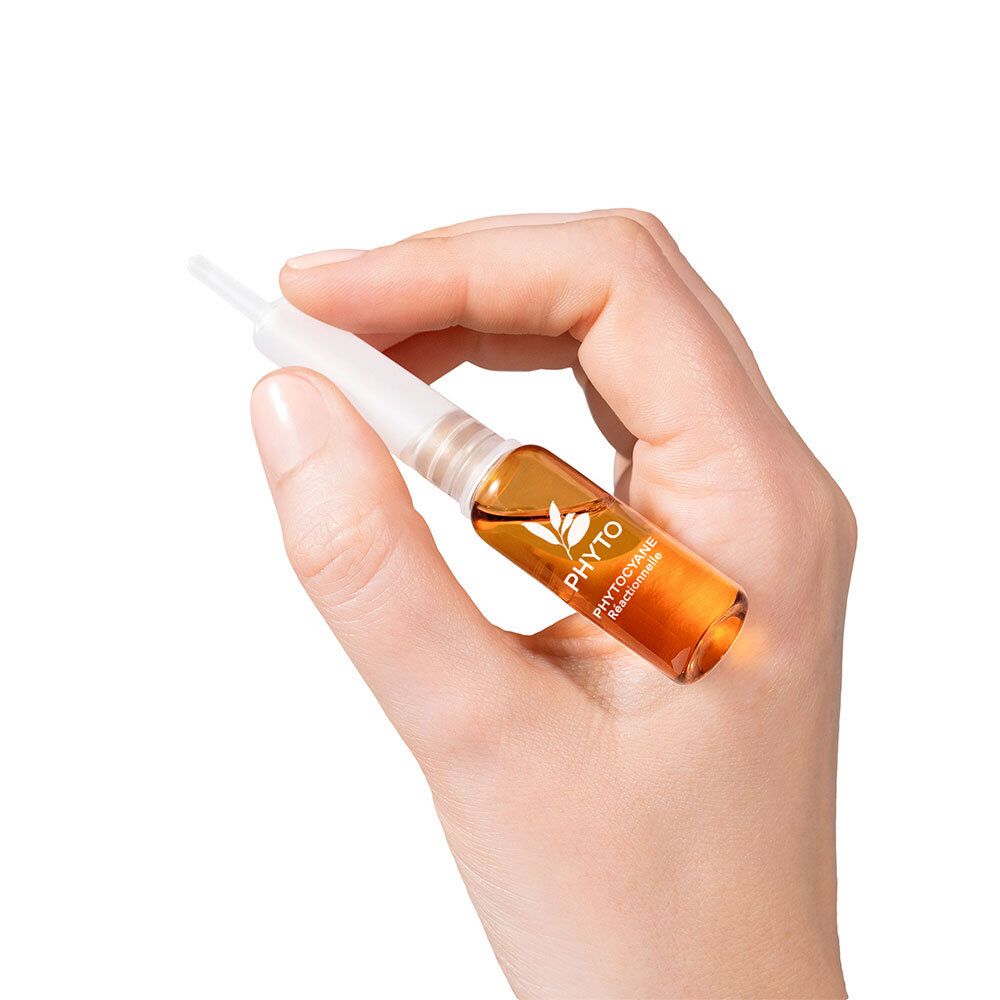 Hand hält eine Phyto Phytocyane Ampulle mit goldener Flüssigkeit.