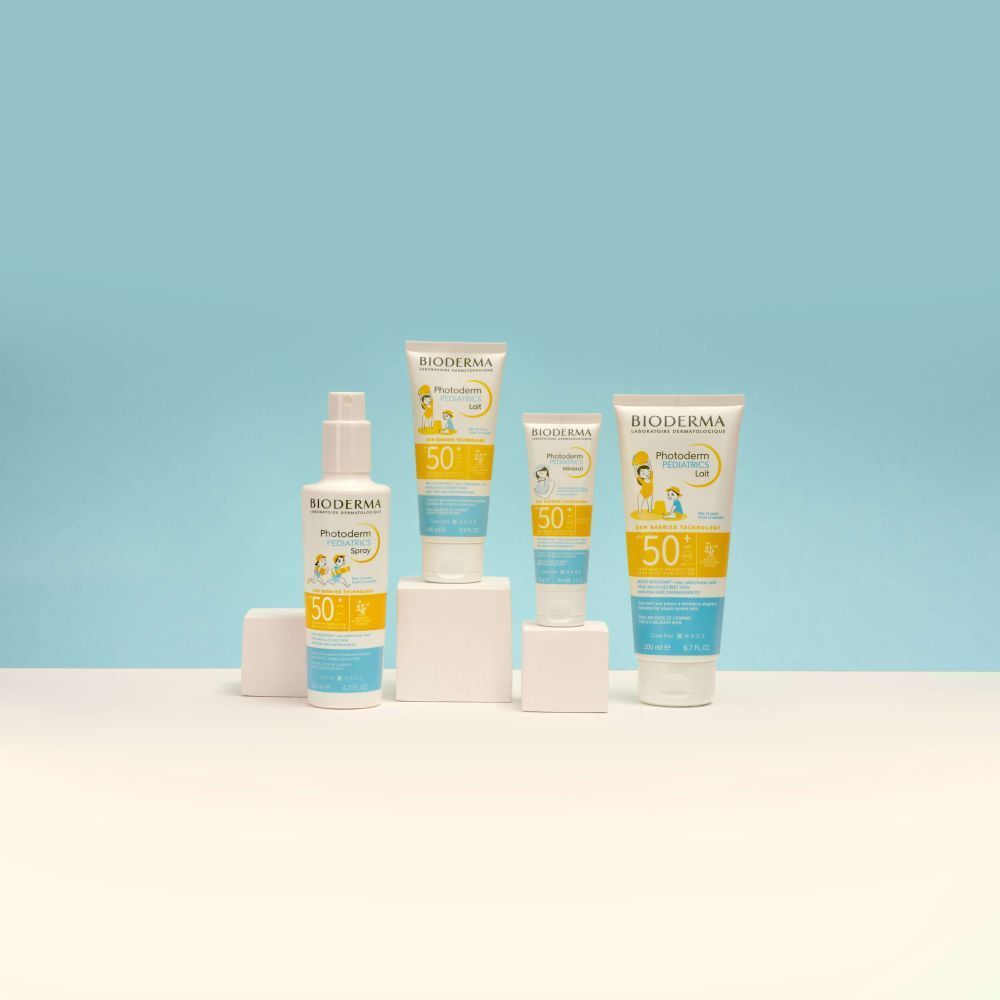 Gamme BIODERMA Photoderm Pediatrics. Différentes tailles et formats, placés sur des socles, sur fond bleu.