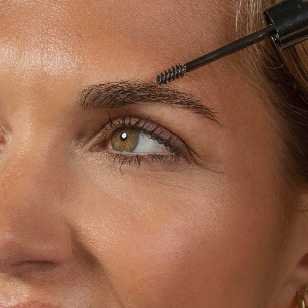 Gros plan d'une femme appliquant le produit sur ses sourcils avec un applicateur.