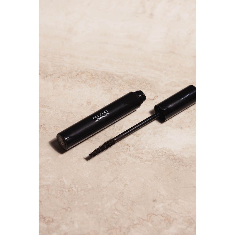 Tube de mascara et brosse sur une surface. Texte: COULEURS DE NOIR. Tube et brosse noirs.