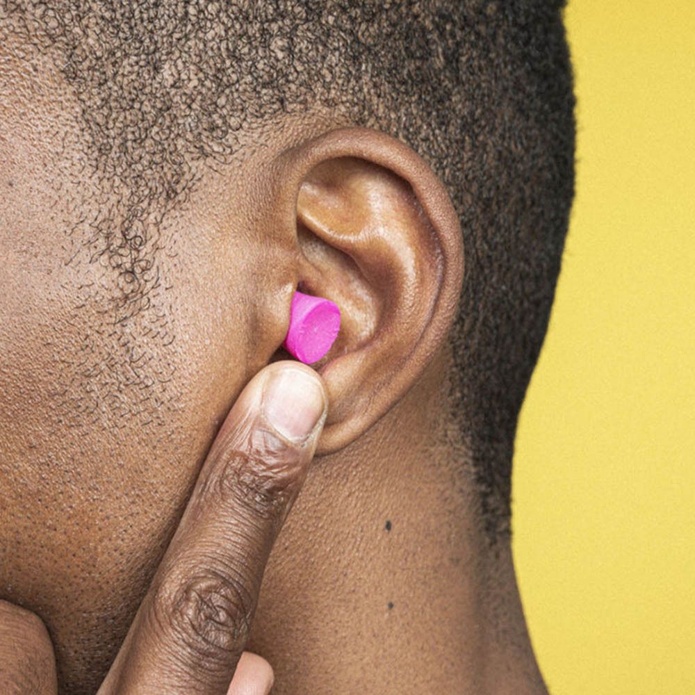 Personne avec un bouchon d'oreille blox® rose dans l'oreille. Fond jaune.