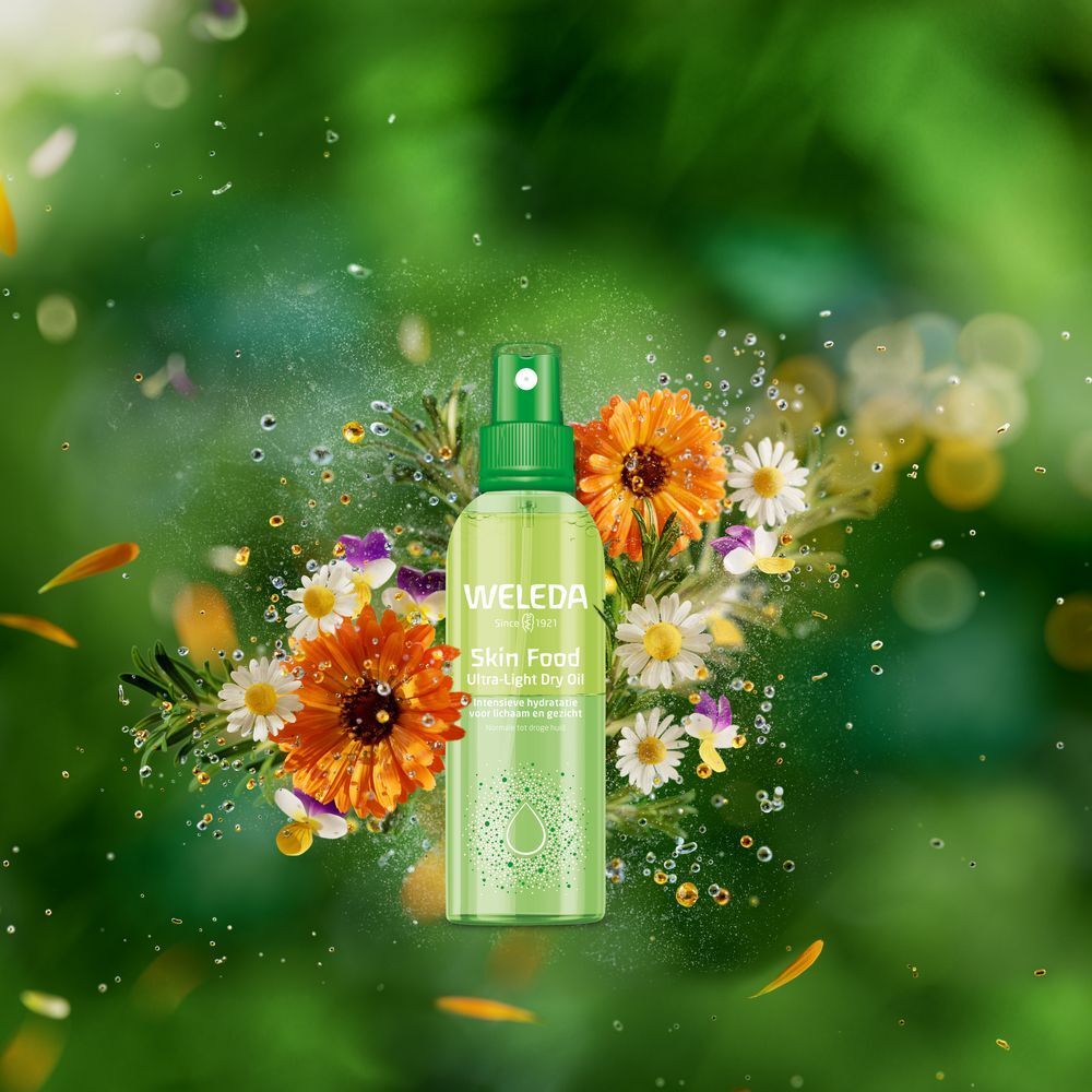 Grüne Sprühflasche mit WELEDA-Logo und Skin Food-Aufschrift. Umgeben von Blumen und Blättern.