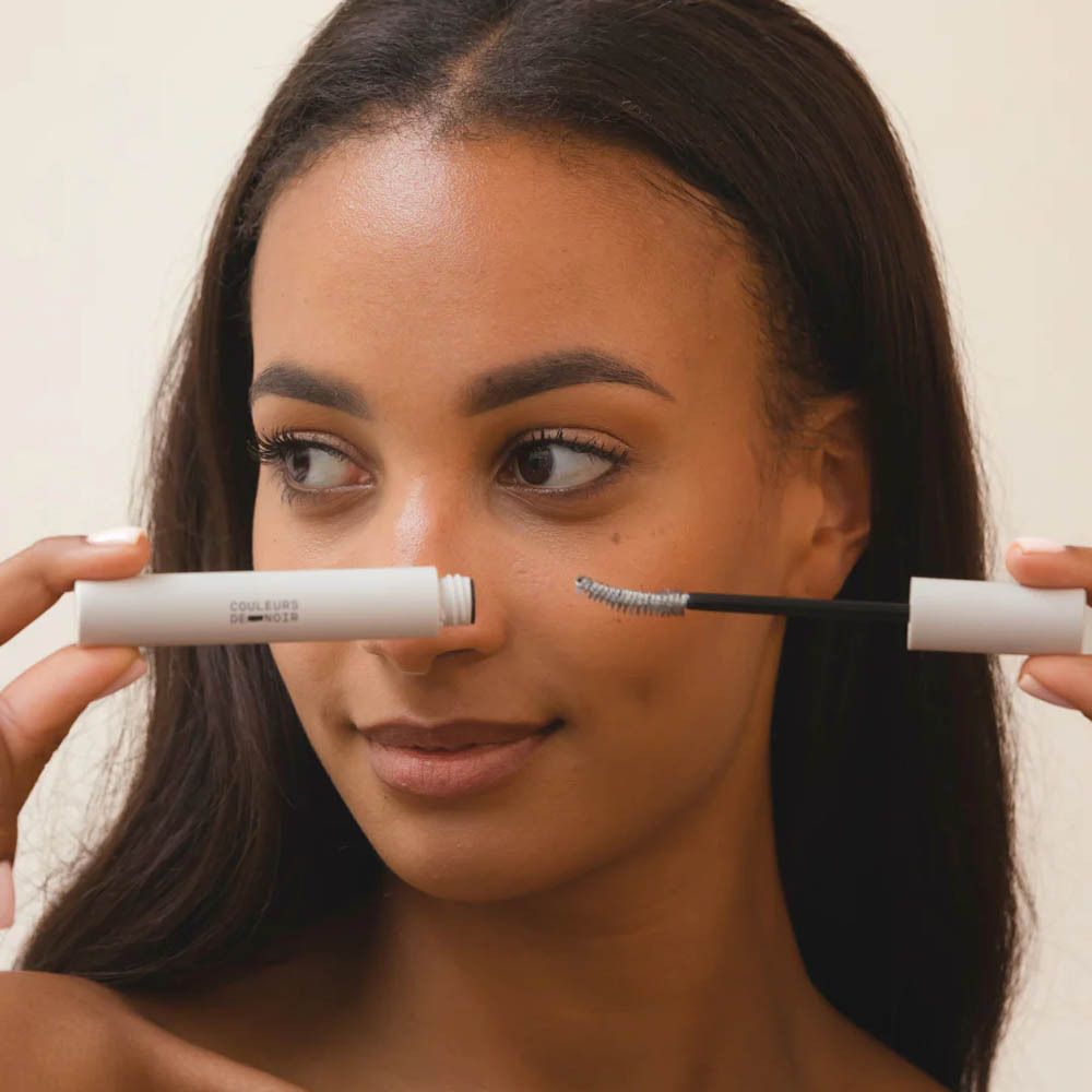 Femme tenant un applicateur de mascara. Contenant blanc, brosse noire.