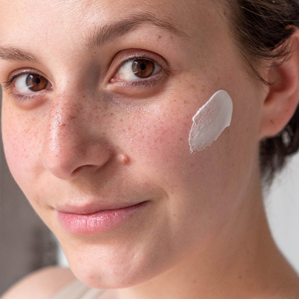 Femme avec de la crème sur la joue. La crème est blanche.