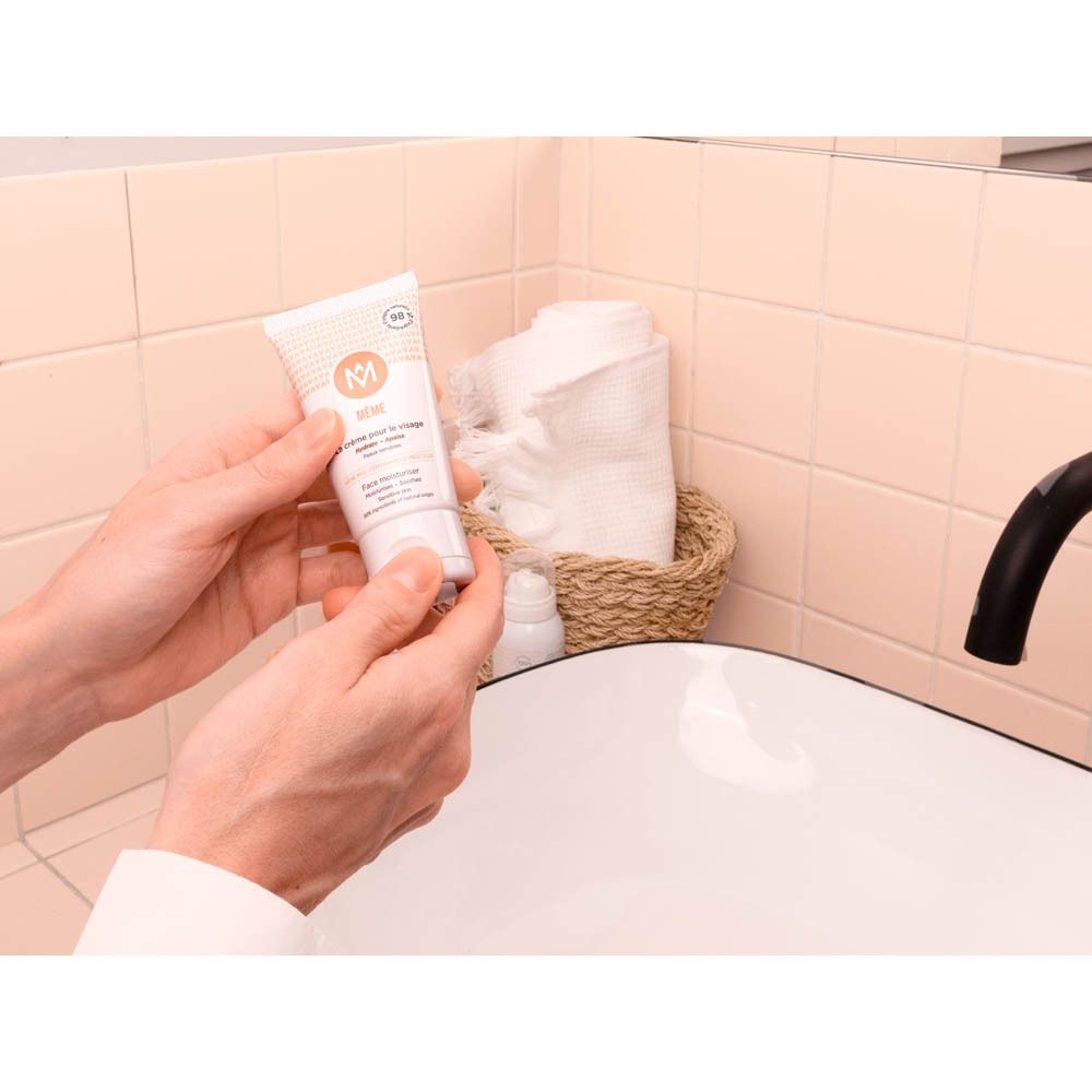 Mains tenant un tube de crème au-dessus d'un lavabo. Inscription : MÊME, La crème pour le visage.