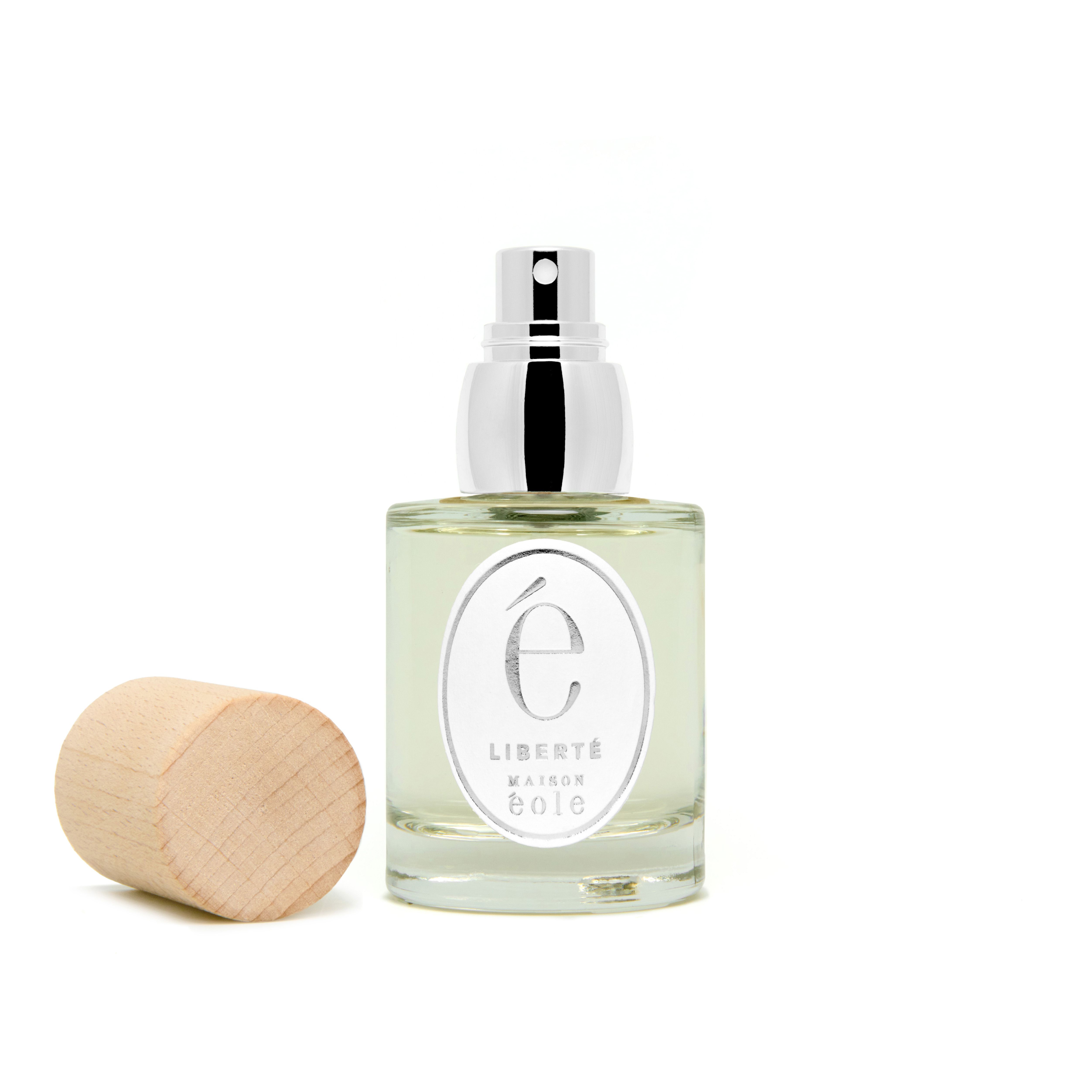 Flacon de parfum avec vaporisateur argenté et bouchon en bois à côté. "Liberté" sur l'étiquette.