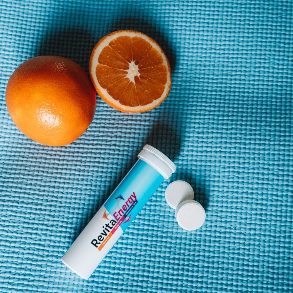 Brausetabletten-Röhre, zwei Tabletten und Orangen auf einer blauen Matte.