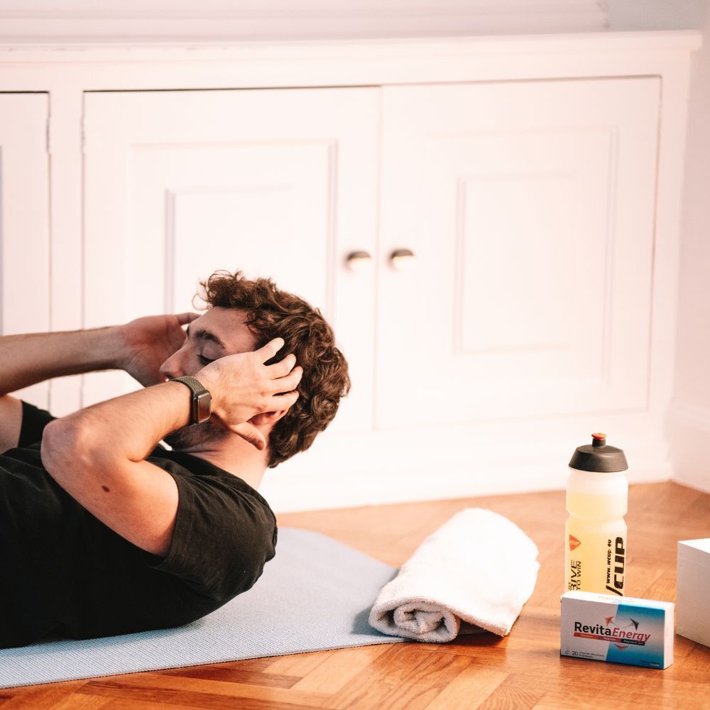 Mann trainiert. Auf einer Matte liegen Handtuch, Wasserflasche und REVITA ENERGIE-Schachtel.