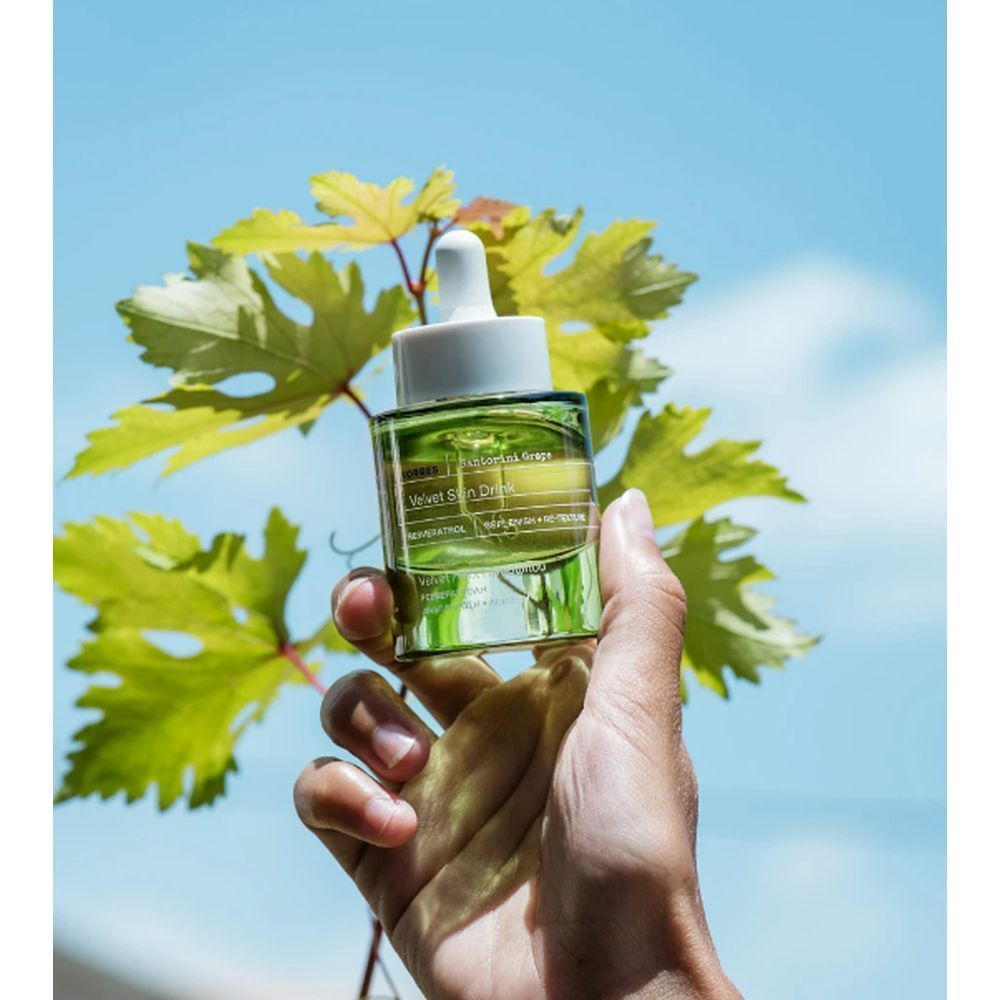 Grüne Glasflasche mit Pipette, gehalten von einer Hand. Hintergrund: grüne Blätter und blauer Himmel.